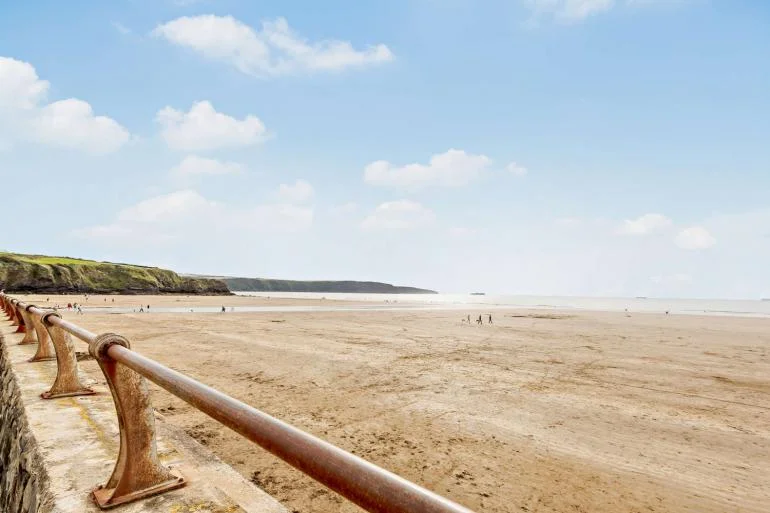 Looking across Broad Haven beach in Pembrokeshire with people walking on the sand in full sunshine.