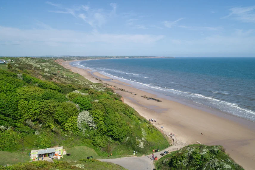 Filey beach on the Yorkshire Coast on a sunny day with gentle waves lapping on the shores.