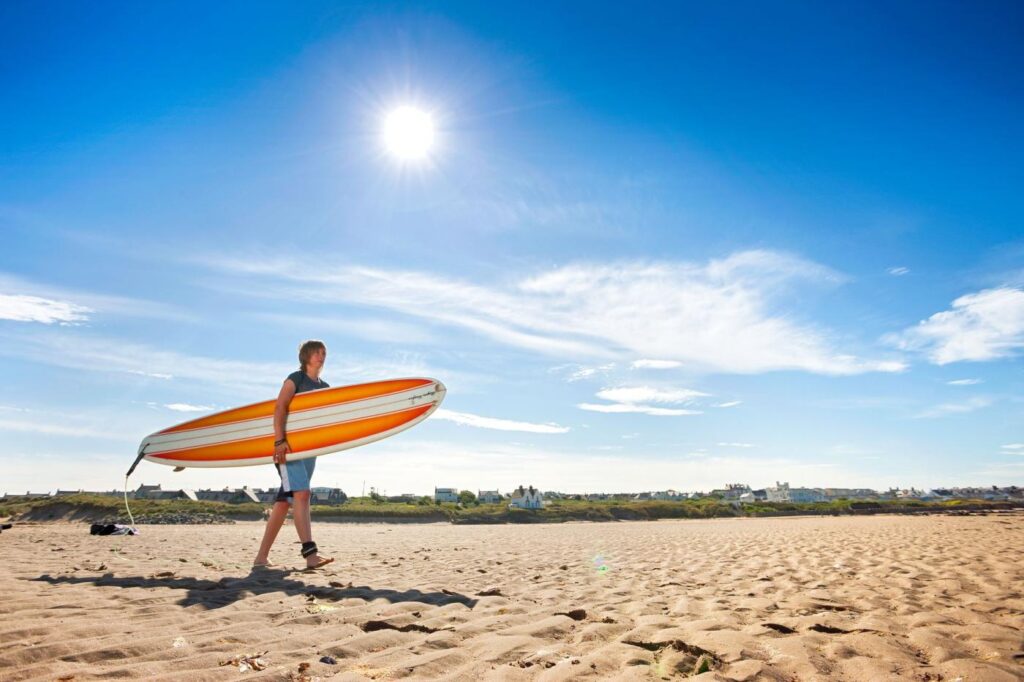 Surfer with long board walking across the beach at Rhosneigr