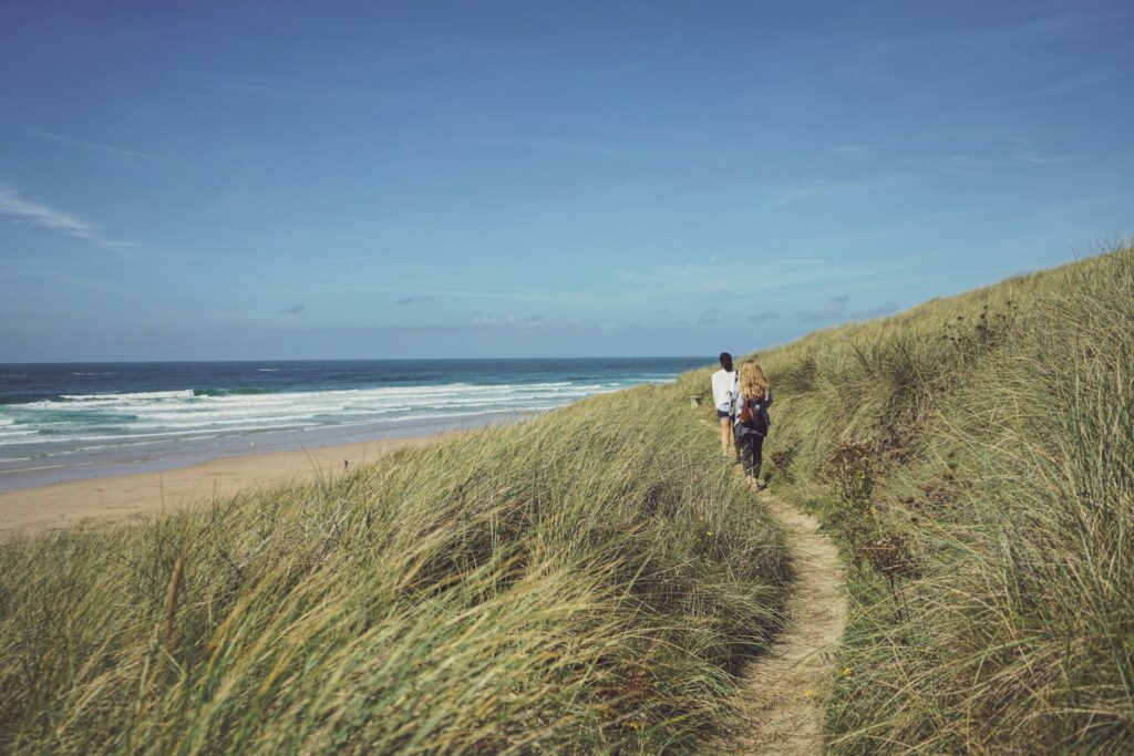 Two people walking along the coast path on Perranporth beach in Cornwall