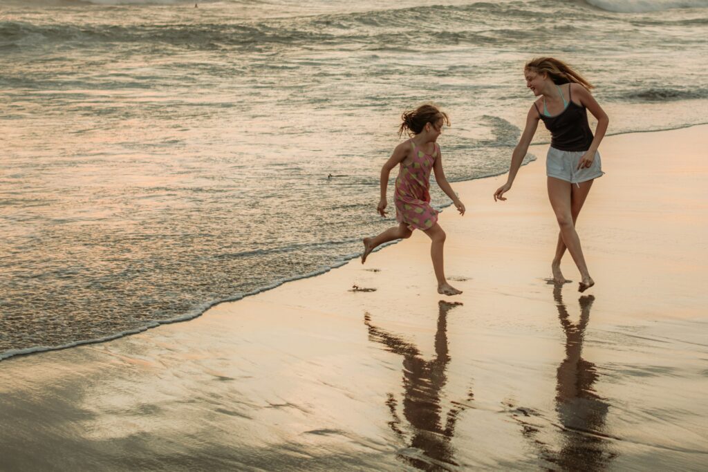 Two girls running barefoot on the wet sand as the sun sets