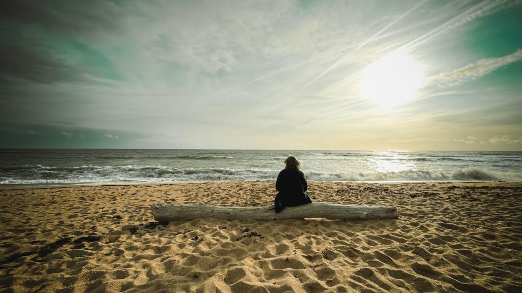Lady sitting on a piece of driftwood looking out to sea