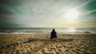 Lady sitting on a piece of driftwood looking out to sea